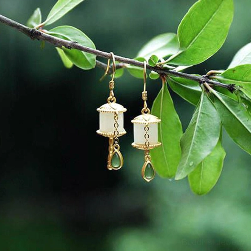 Jade prayer wheel dangle earrings top-down view on white ceramic plate backdrop with teardrop charm design, emerald green and gold