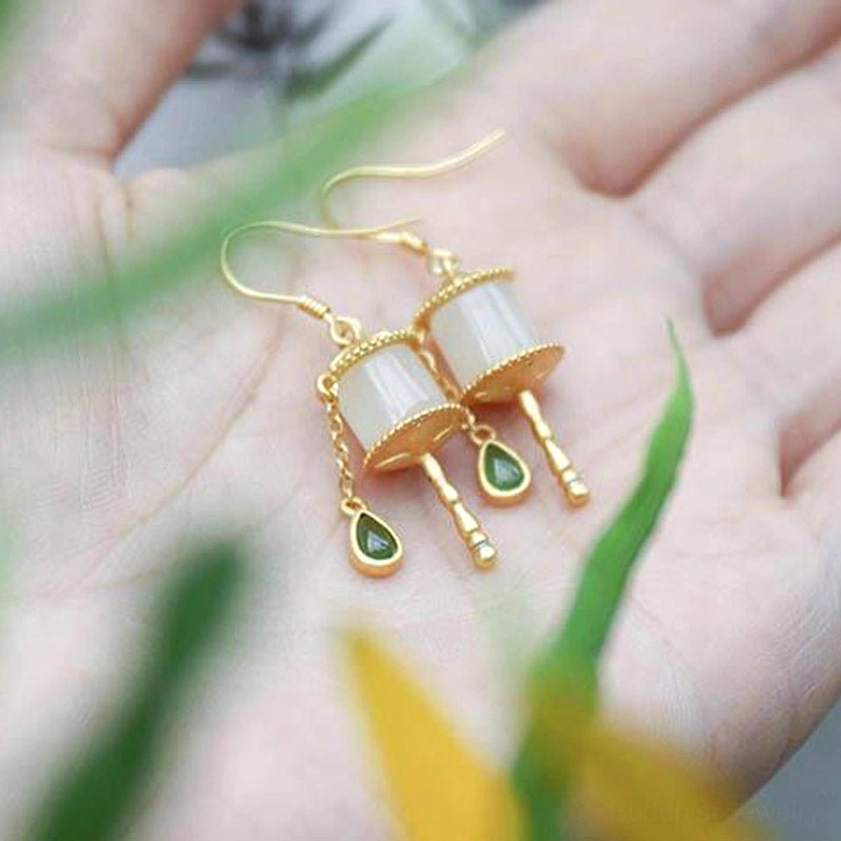 Jade prayer wheel drop earrings top-down view resting on human palm, hook-style dangle design with milky white jade and gold accents