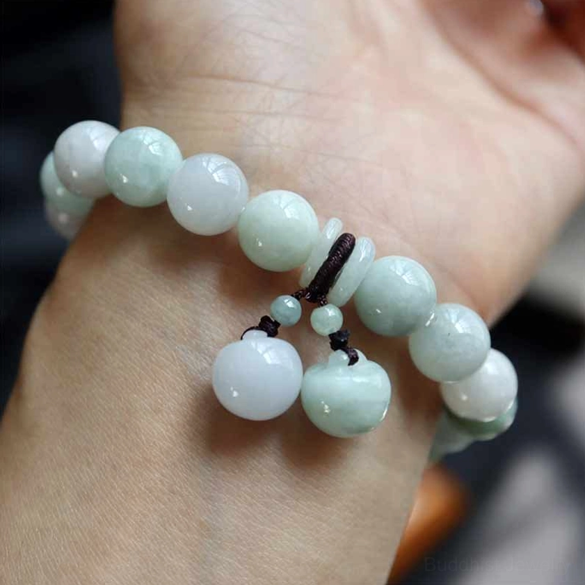Close-up wrist view of natural jade bead bracelet with solid light green jade beads and round jade pendants on brown cord worn on human wrist