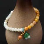 Natural jade and quartzite beaded bracelet with green lotus pod charm, displayed on ceramic vase showing warm-toned and white jade beads