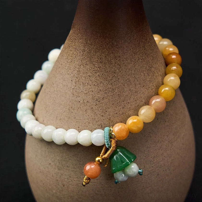 Natural jade and quartzite beaded bracelet with green lotus pod charm, displayed on ceramic vase showing warm-toned and white jade beads