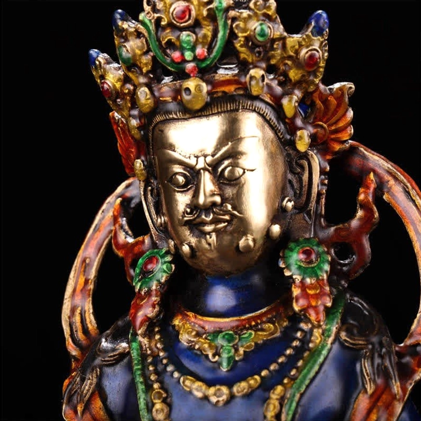 Jambhala deity crown and face close-up showing gem-inlaid ornate crown and colorful enamel accents with gilt details