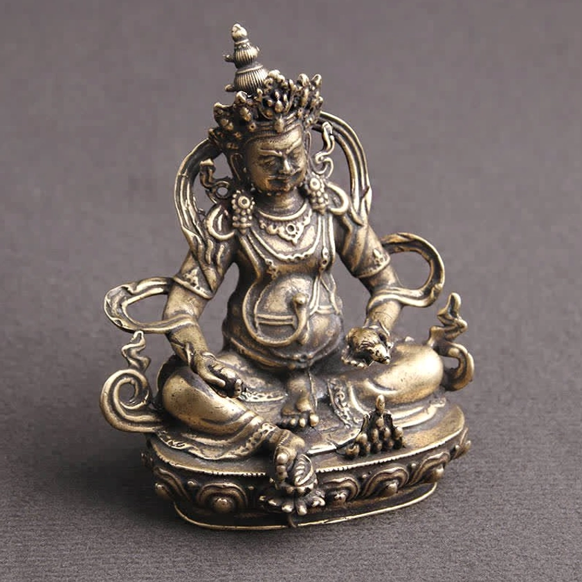 Jambhala Buddha figurine three-quarter side angle showing carved details, aged metal texture, and intricate ornamental jewelry