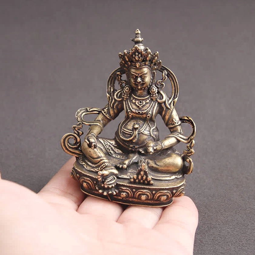 Palm-sized Yellow Jambhala Buddha copper figurine held in hand for scale, showing fine details and bronze patina