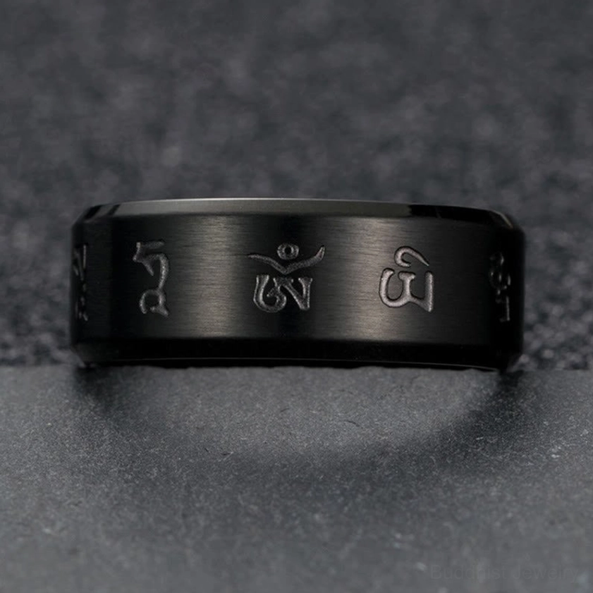 Direct overhead flat lay of black titanium steel mantra ring with prominent hand-engraved sacred mantras and solid band structure