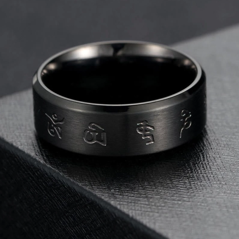 Top-down overhead view of black titanium steel Jambhala mantra ring, displaying engraved sacred symbols and polished band