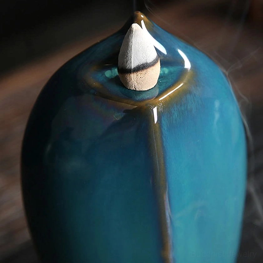 Jar shaped backflow incense burner close-up top view with teal glazed ceramic body and incense cone with slight smoke emission