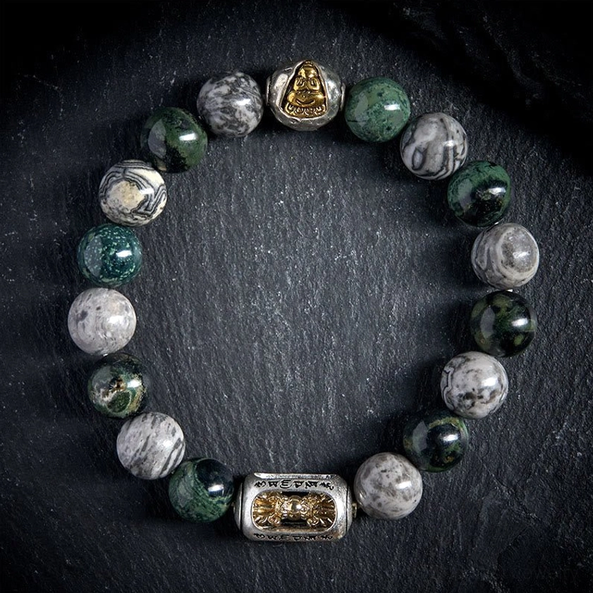 Natural grey jasper beads with engraved mantra charm and gold Buddha bead on black velvet background, close-up detail shot