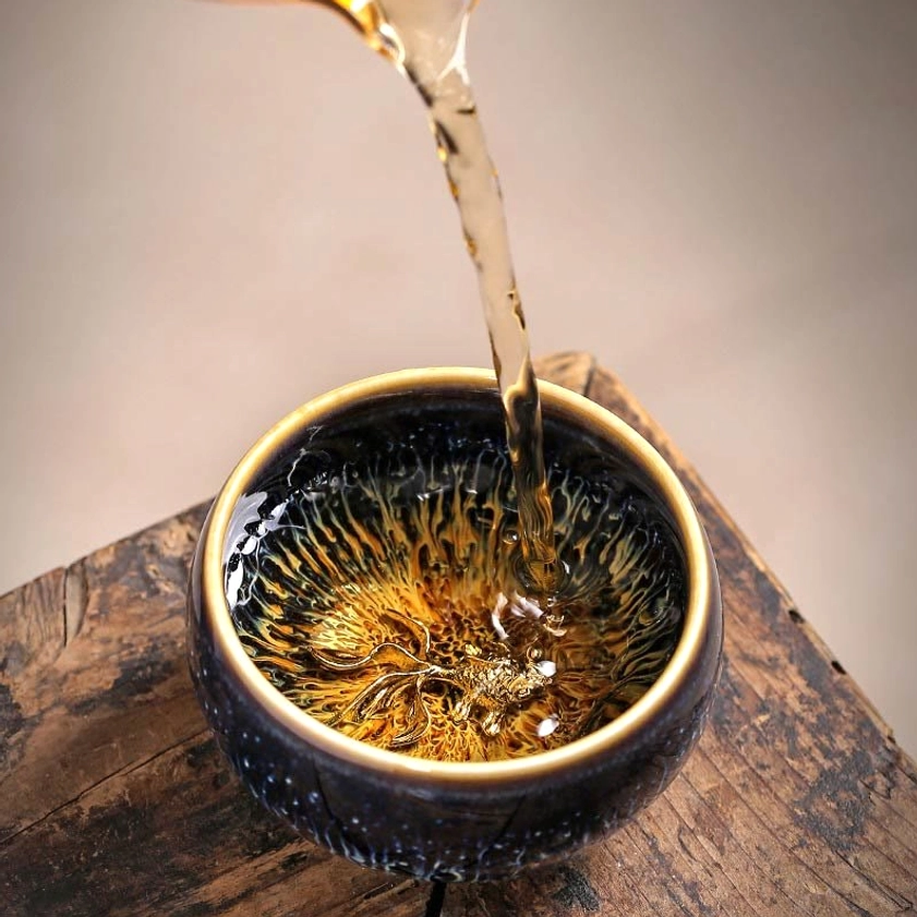 Jian Zhan tea cup during tea pouring, showing functional use and gold koi fish ornament inside the cup with steaming water