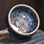 Handmade Jian Zhan ceramic tea cup with koi fish ornament, close-up interior view showing blue-yellow glazed pattern and gold rim