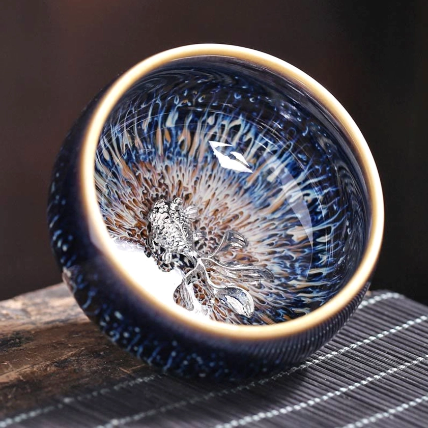 Handmade Jian Zhan ceramic tea cup with koi fish ornament, close-up interior view showing blue-yellow glazed pattern and gold rim