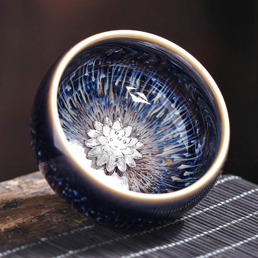 Jian Zhan tea cup with lotus flower ornament, close-up interior showing blue-yellow glazed pattern and gold rim on wooden table