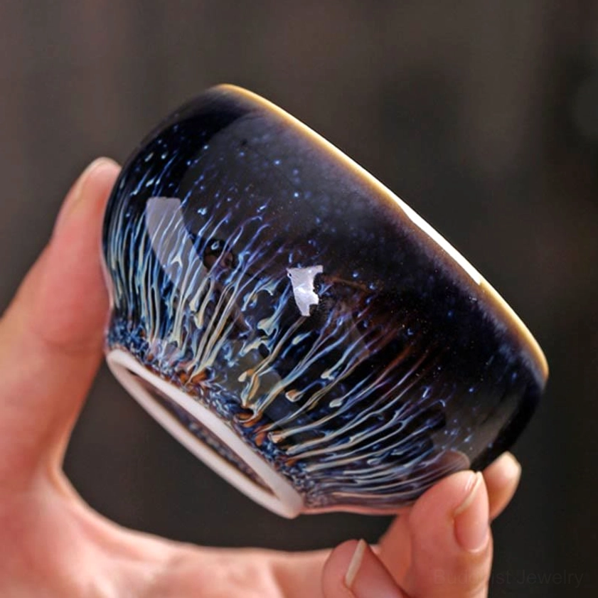 Side profile of handmade Jian Zhan tea cup showing blue-white streaked glaze pattern, glossy finish, and gold rim detail