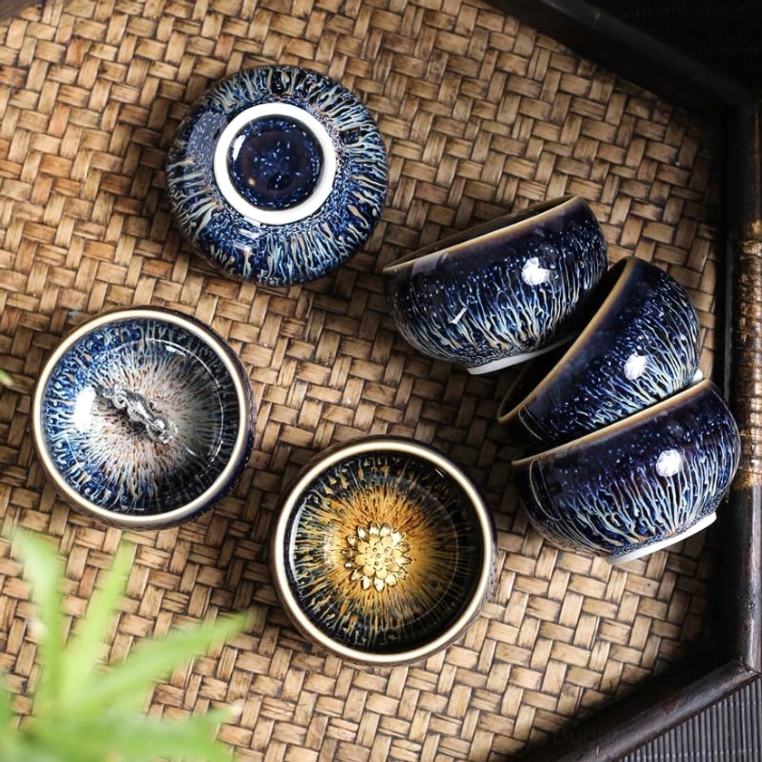 Collection of multiple Chinese zodiac Jian Zhan tea cups arranged on woven rattan tray, showing various celestial glaze patterns and designs
