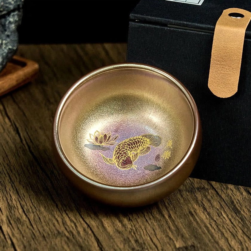Jianzhan ceramic kung fu tea cup with warm bronze-gold finish and koi lotus pattern, displayed with velvet-lined gift box