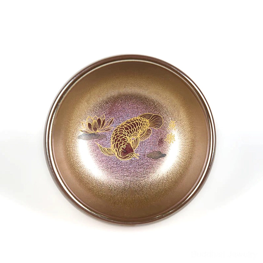 Jianzhan tea cup with bronze rim and purple inner glaze showing full koi lotus pattern on bottom, direct top-down view on white background