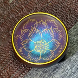 Handmade Jianzhan lotus ceramic tea cup with purple-blue gradient and gold gilded petals, overhead view on woven fabric