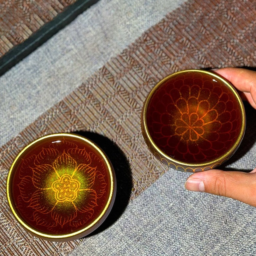 Reddish-brown Jianzhan lotus teacups with gold rim and gilded lotus motifs, one held in hand to show scale and craftsmanship