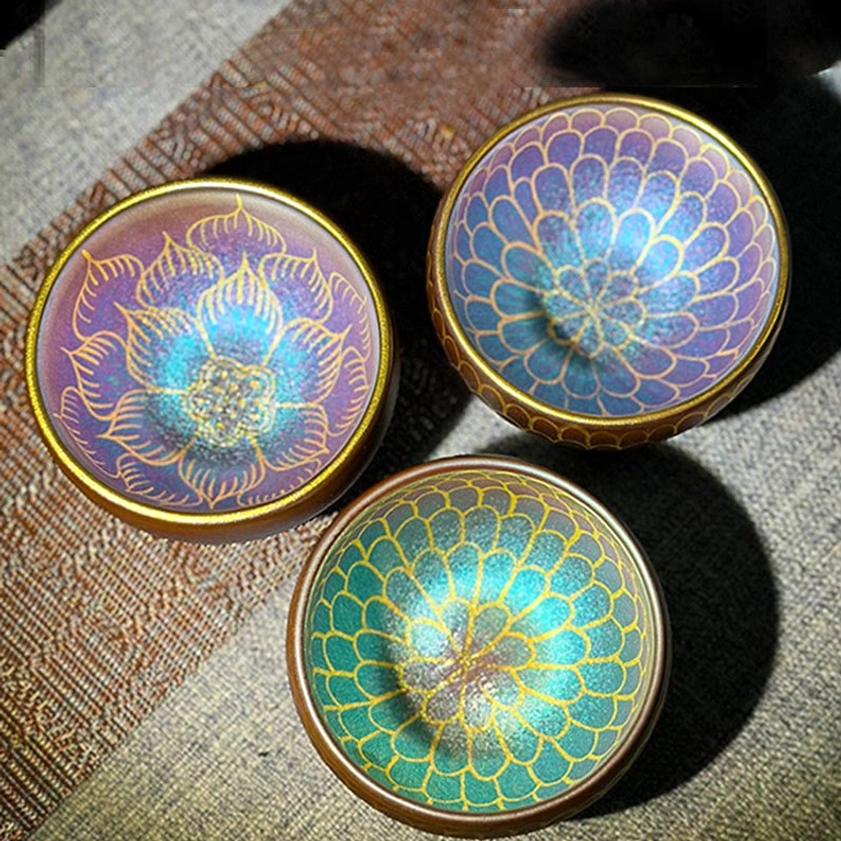 Three artisan Jianzhan lotus teacups in blue green, blue pink, and blue purple gradient colors with gilded designs, flat lay arrangement