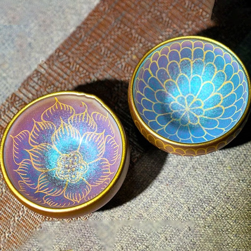 Two handmade Jianzhan lotus ceramic teacups with purple-brown body and gold gilded lotus flower patterns, elevated perspective