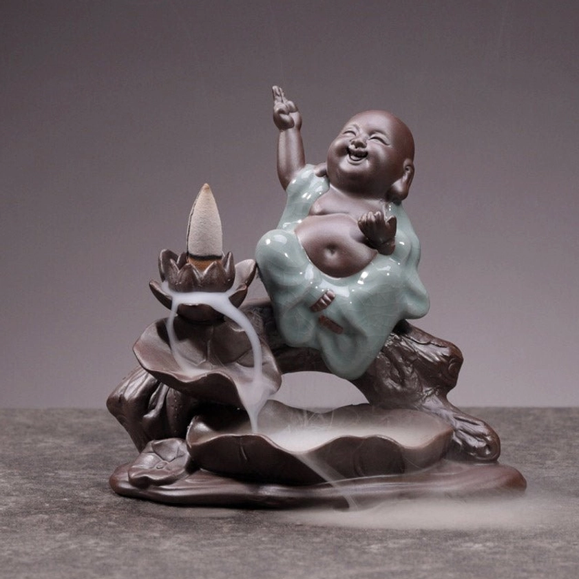 Joyful little monk ceramic backflow incense burner, right three-quarter angle, indoor tabletop display, dark brown ceramic with celadon outfit, visible incense smoke effect