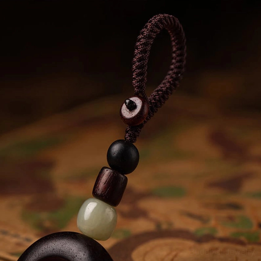 Buddhist keychain lanyard close-up showing stacked wooden beads, black spacers, and light green jade beads on braided cord