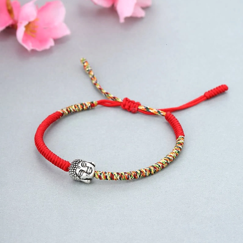 Handwoven Buddhist lucky string bracelet with multicolor threads, red cord and silver Buddha bead, flat lay view