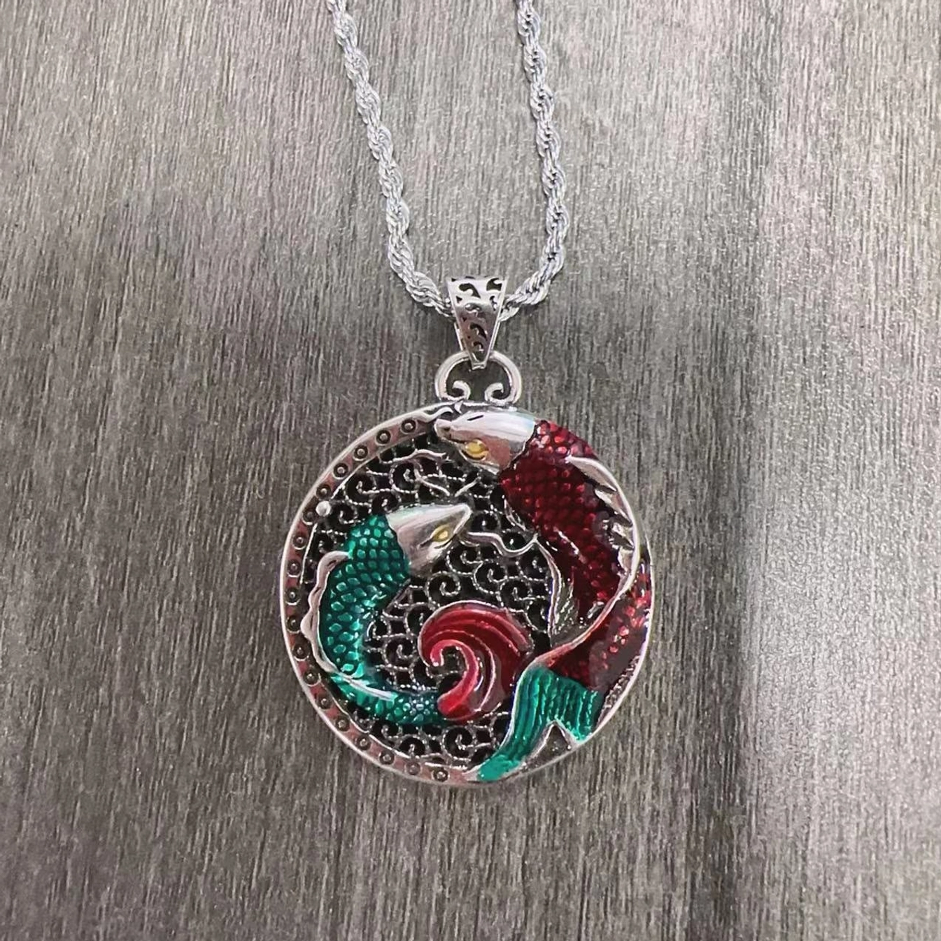 Silver twisted chain koi fish pendant necklace with polished enamel Buddhist design on wooden surface