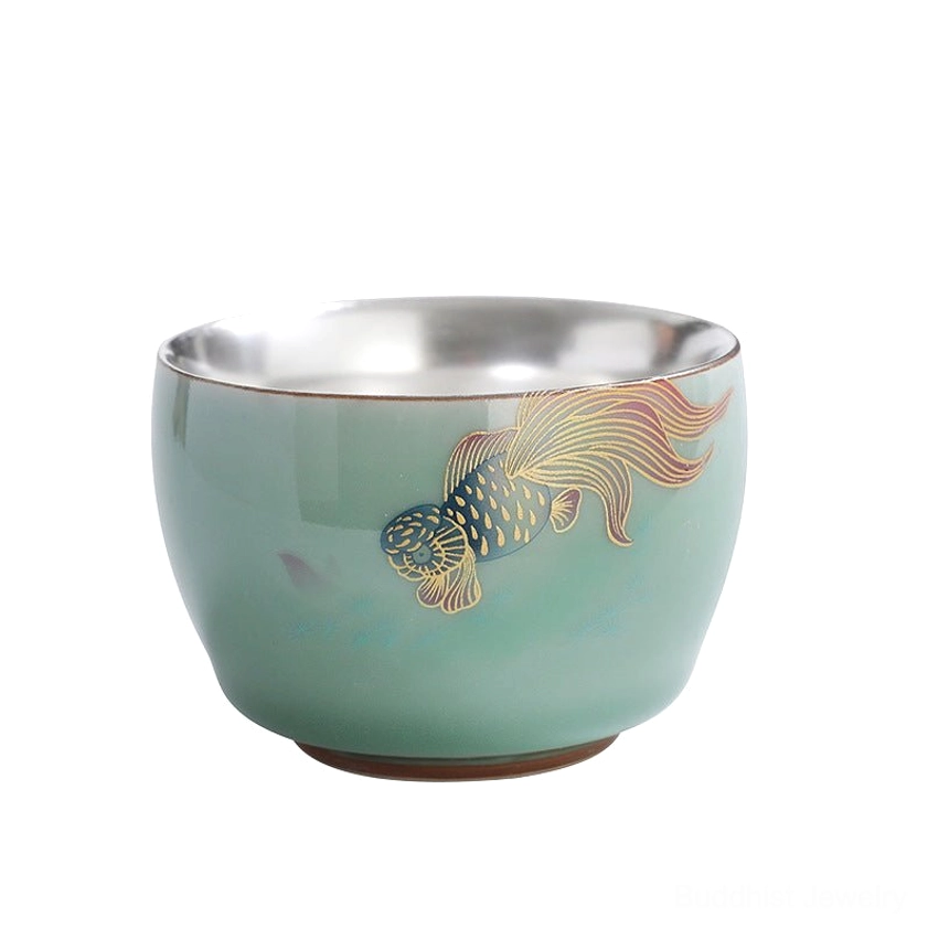 Isolated product shot of celadon Buddhist tea cup with koi fish pattern and silver interior on white background