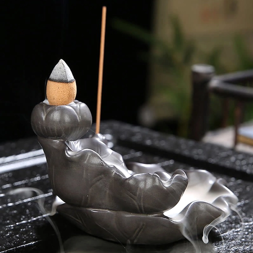 Profile view of ceramic koi fish lotus incense burner with slight smoke at base on blurred outdoor background