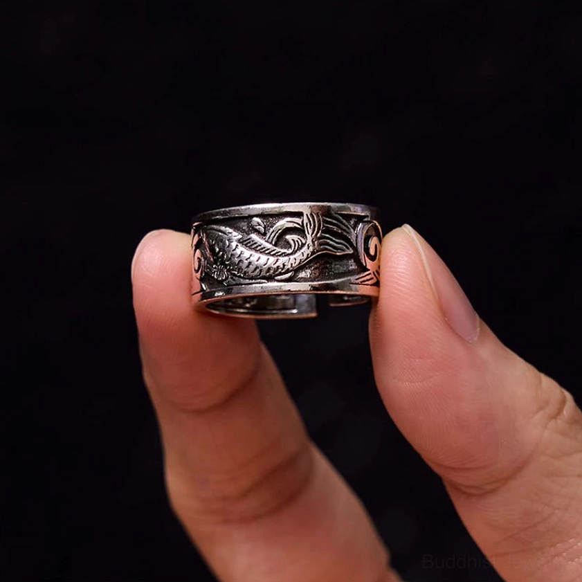 Koi fish open band ring held by fingertips on black background, embossed carp design with adjustable fit