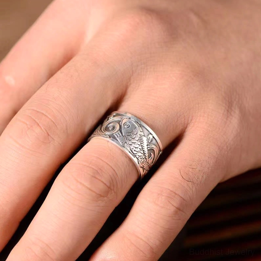 Koi fish carved copper ring side close-up worn on hand over dark wooden table, antique silver look with detailed fish carving