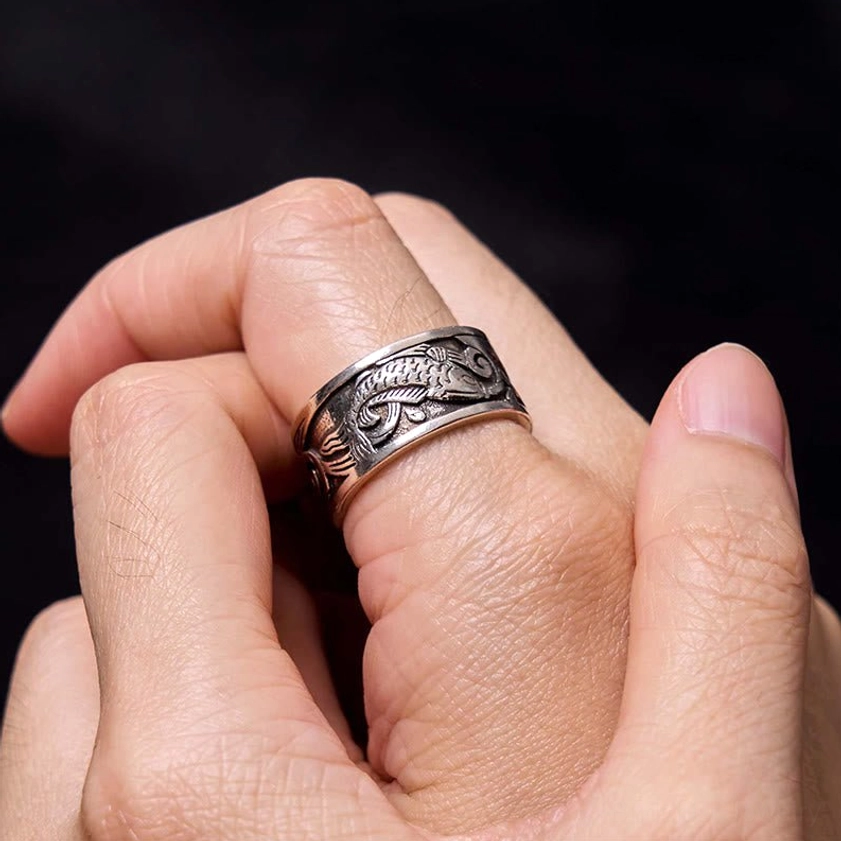 Koi fish buddhist ring worn on middle finger against black background, vintage silver finish showing hand-carved carp motifs
