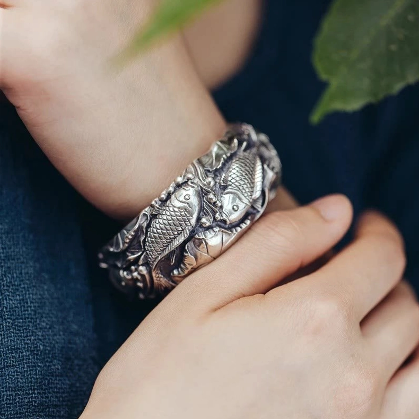Double koi embossed silver cuff bracelet detail shot showing aged patina and Buddhist symbols