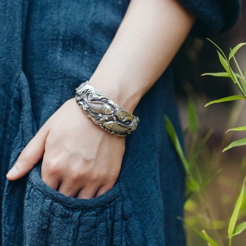Two-tone koi lotus bracelet with gold accent details worn outdoor with green plants background