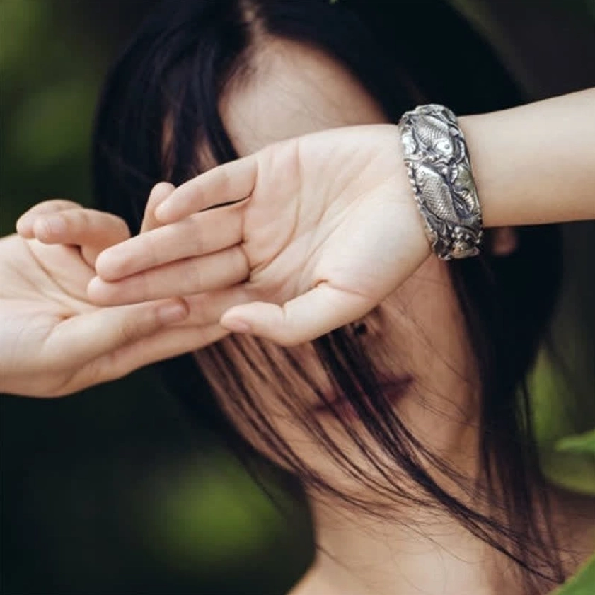 Close-up of vintage silver koi lotus bracelet on model wrist with natural outdoor lighting