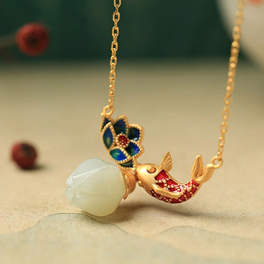 Buddhist jade koi fish lotus pendant necklace overhead view with reversed koi design and gold chain on decorative table