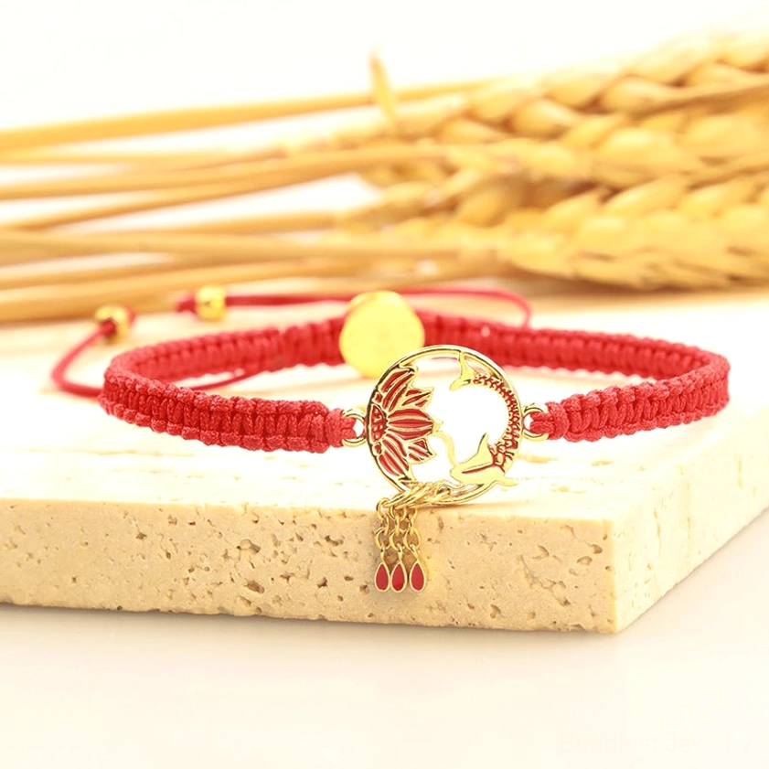 Koi lotus lucky red bracelet displayed on wooden block with gold hardware and red drop pendants, flat lay