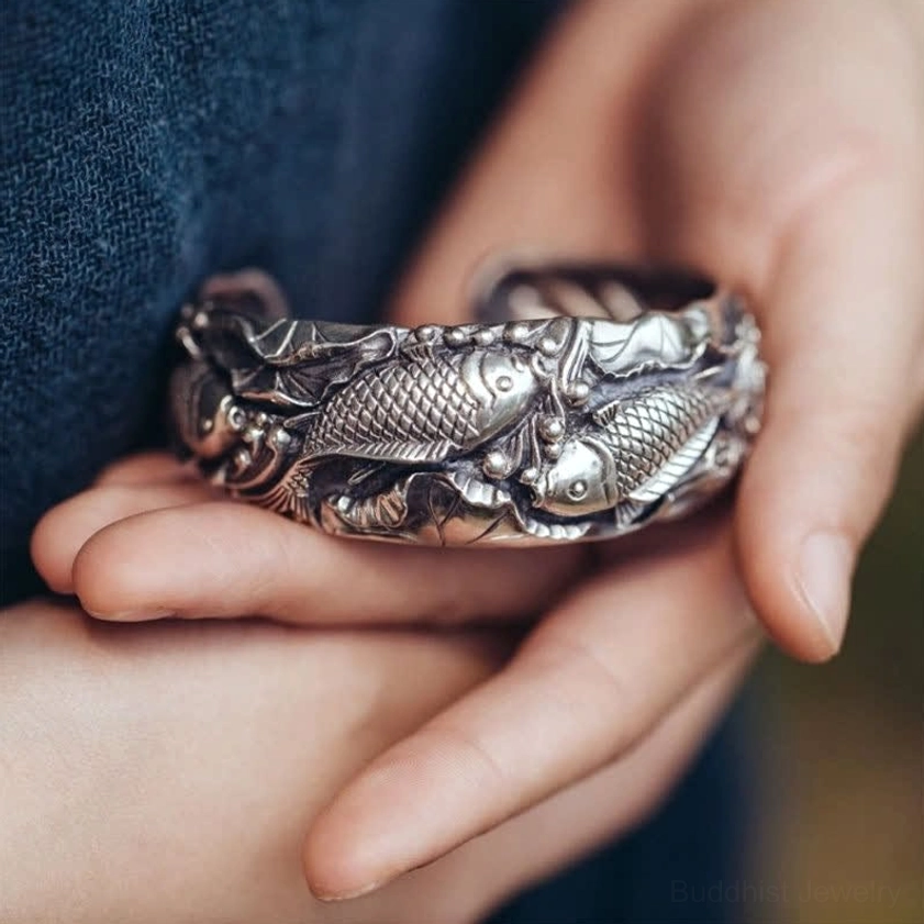 Koi fish lotus silver cuff bracelet with embossed prosperity symbols worn on wrist with blue linen