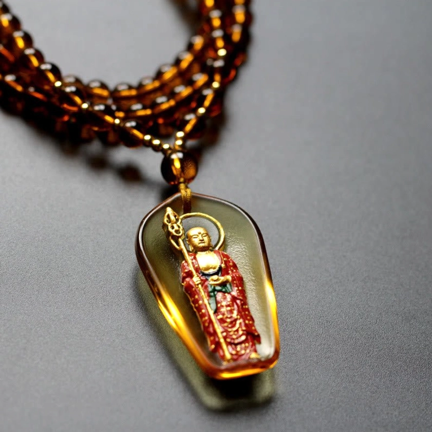 Amber translucent Ksitigarbha Buddha seated liuli crystal pendant with gilded red Buddha figure, front close-up view with beaded necklace