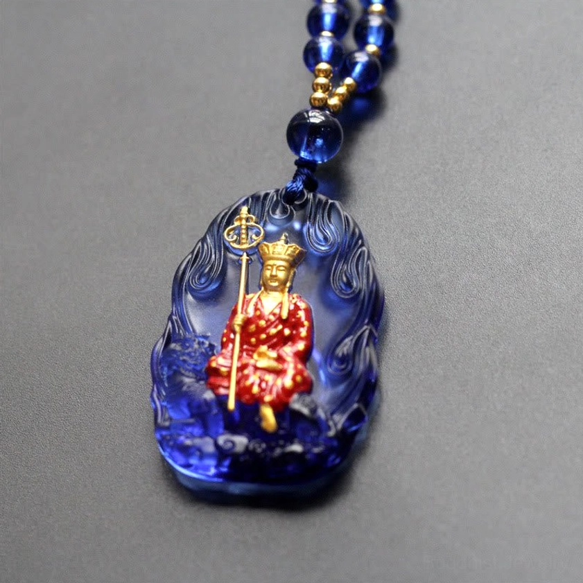 Deep blue translucent Ksitigarbha Buddha liuli crystal pendant with seated gilded Buddha and khakkhara, front close-up with blue beaded necklace