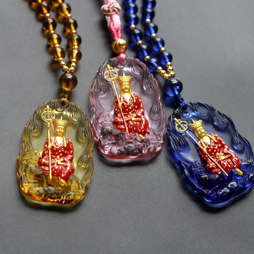 Three Ksitigarbha Buddha liuli crystal pendants in amber, purple, and blue colors with seated Buddha figures, flat lay comparison view