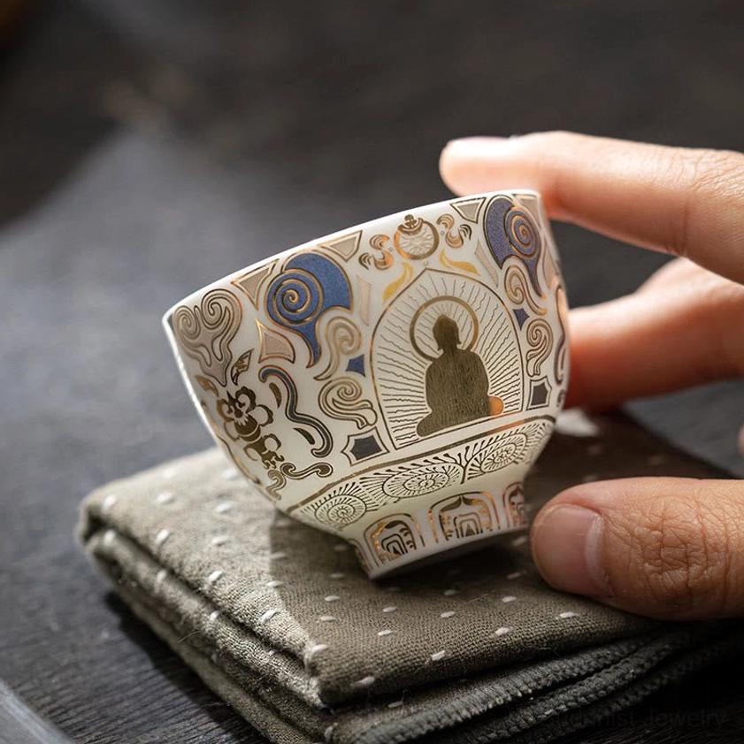 Low angle side view of handcrafted white porcelain Buddha tea cup with footed base and auspicious cloud patterns, displayed on dark table with linen cloth