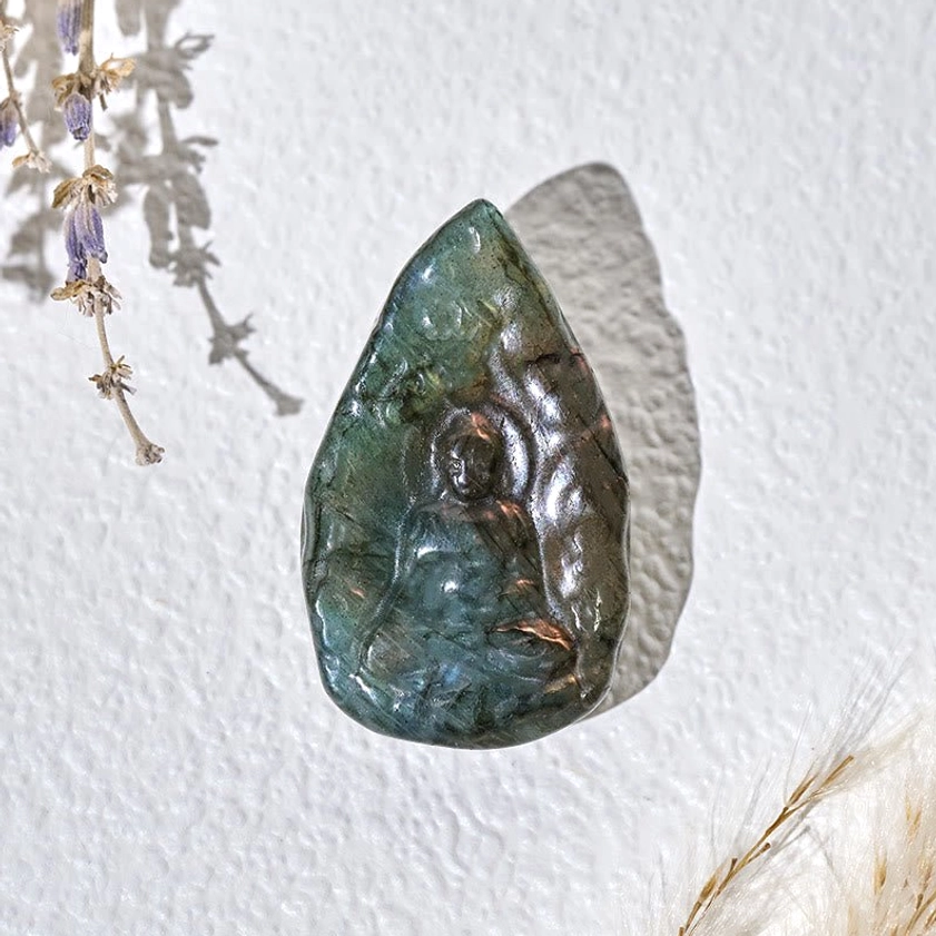 Hand-carved labradorite Buddha figurine displayed on minimalist background, showcasing carved Buddha relief and polished iridescent labradorite finish