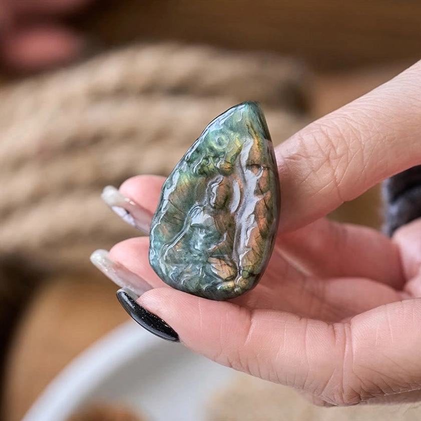 Handheld labradorite Buddha carving with multi-color iridescent shimmer, close-up side view revealing Buddha pattern and natural stone texture