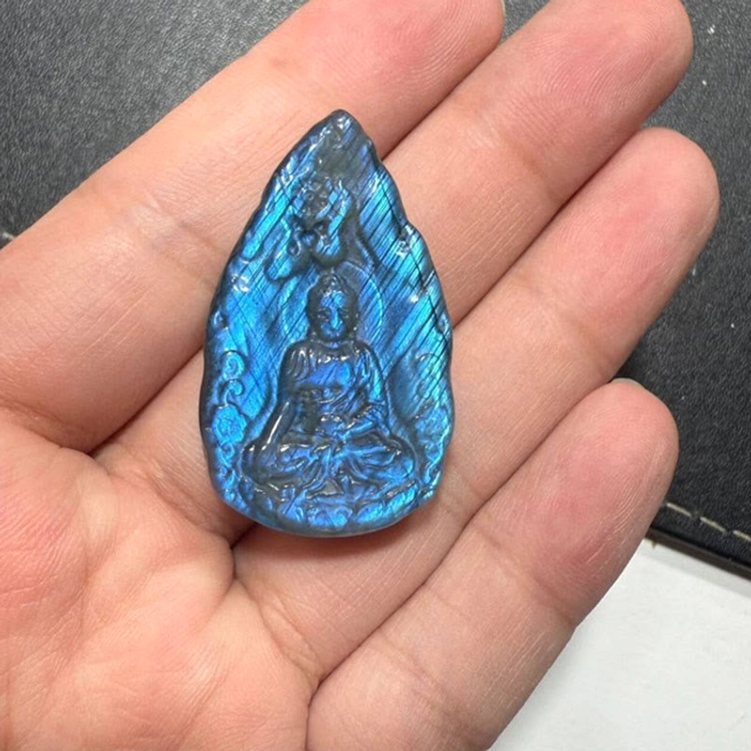 Deep blue labradorite Buddha statue with vivid iridescent shimmer, hand-held close-up showing detailed seated Buddha carving and intense blue glow