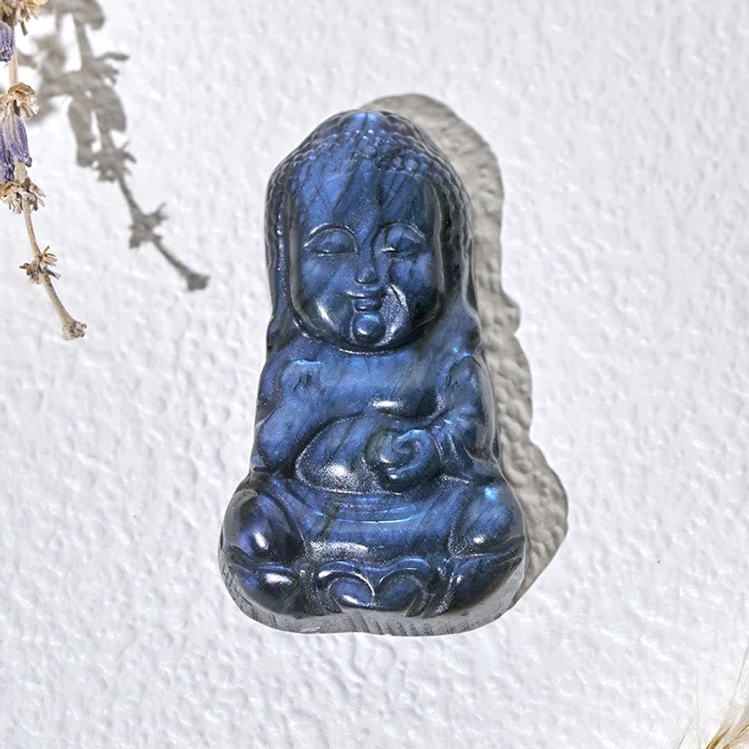 Overhead flat lay of carved labradorite Buddha statue in seated meditation pose on textured background
