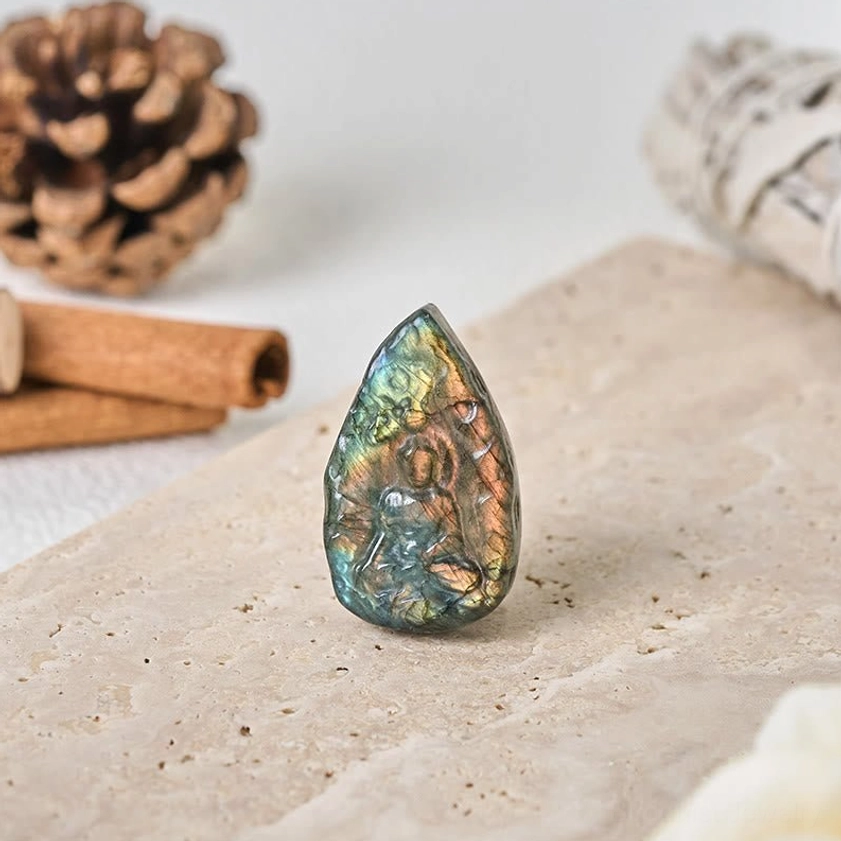 Labradorite Buddha teardrop ornament on warm-toned tabletop display, carved seated Buddha figure with iridescent labradorite finish