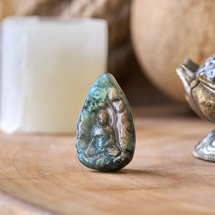 Natural labradorite Buddha statue with blue-green iridescent glow, front view on vintage tabletop display showing seated Buddha carving