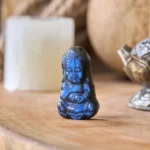 Handcarved labradorite Buddha figurine with deep blue iridescent flash on wooden tabletop display